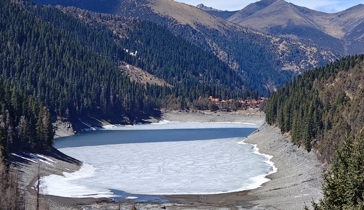 Partly frozen Sarljok Tso surrounded by forested mountain slopes during winter fieldwork.